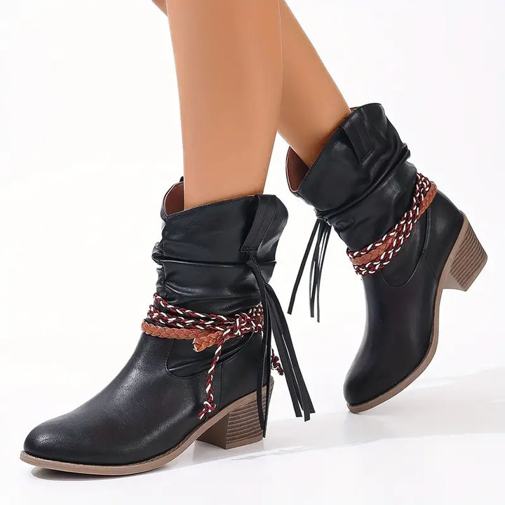 Front view of ankle boot with braided wraps, tassels and shaped opening, black